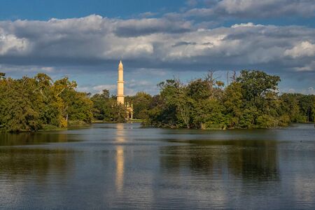 Lednice Minaret - Romantic lookout tower in Castle Park (UNESCO). A tower on the banks of Castle Pond, surrounded by trees, and a blue sky with cloudsのeditorial素材