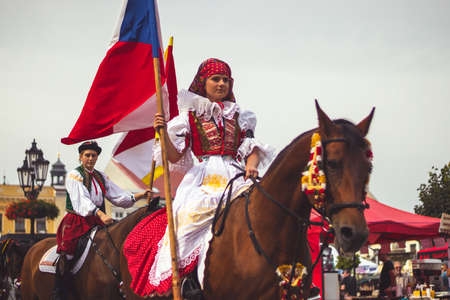 Kromeriz / Czech republic, Slavic harvest festival in Moravia (Czech Republic). Girl in traditional costume with flag rides a horse at the head of the parade on the historic squareのeditorial素材