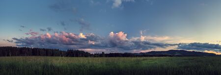 panorama landscape at sunset - meadow, forest and hills and clouds illuminated by the setting sunの写真素材
