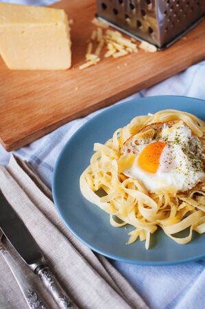 Angle view of pasta with egg, cheese and herbs. Mediterranean supper with cutlery on checked towel.の写真素材