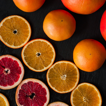 Citrus flatlay on dark rustic background. Sliced and whole oranges and grapefruits.