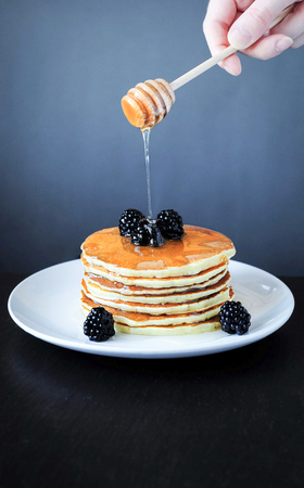 Angle view Stack of pancakes on white plate with blackberry and flowing honey on it. Warm still...