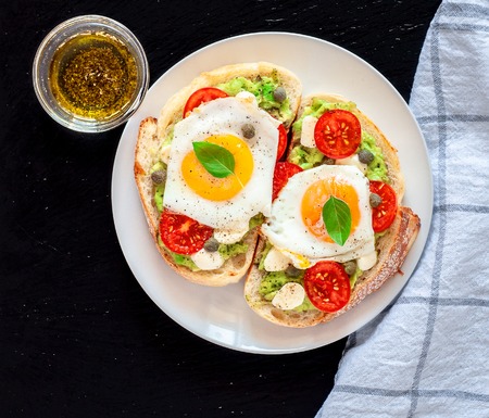Sandwich toasts with agg, tomatoes cherry, mozzarella, avocado, basil and olive oil. Top view on a dark stone background. Flat lay.の写真素材