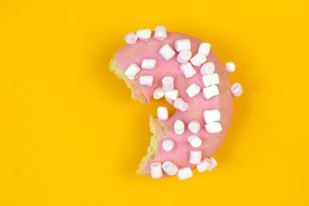 Sweet pink donut bited on yellow background. Dessert foodの写真素材