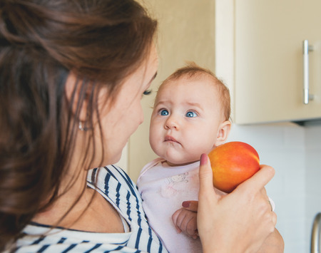 Young mother feeding baby a red apple. Funny baby girl trying to eat apple.の写真素材