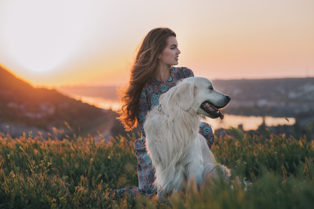 Young woman sitting with her dog enjoying sunset.の写真素材