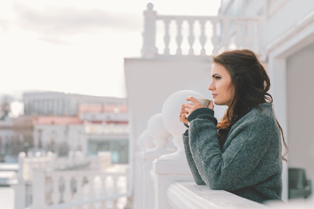 Beautiful woman relaxing and drinking coffee on the balcony in the morningの写真素材