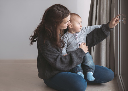 Beautiful young mother having fun with her baby at home on the floor near windowの写真素材
