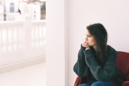 Beautiful woman in gray sweater sits on a chair on balconyの写真素材
