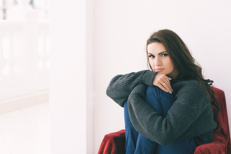 Beautiful woman in gray sweater sits on a chair on balconyの写真素材