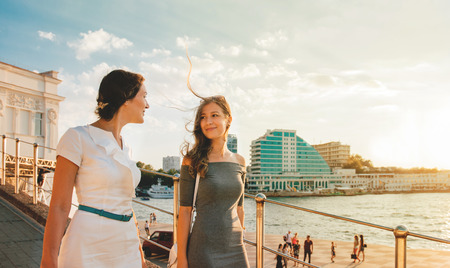 Mother and teen daughter walking, talking and smiling on the street. Sunset light.の写真素材