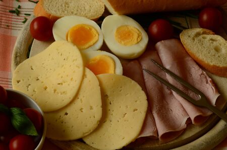 Cooked eggs, slices of salami and cheese with baguette and cherry tomatoesの写真素材