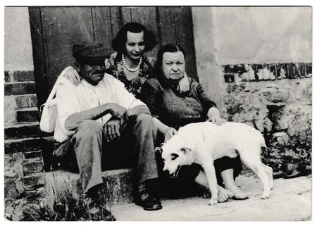 THE CZECHOSLOVAK SOCIALIST REPUBLIC - CIRCA 1960s: Retro photo shows rural people sit on a doorstep with dog. Black & white vintage photographyのeditorial素材