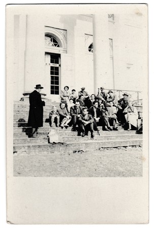 KUTNA HORA, THE CZECHOSLOVAK SOCIALIST REPUBLIC - APRIL 25, 1954: Retro photo shows a group of people sits on stairs outside. Vintage black & white photography.のeditorial素材