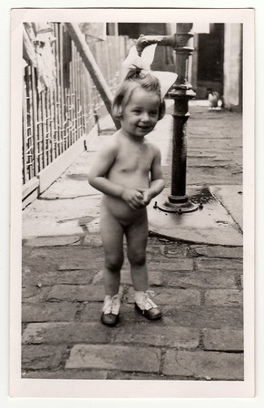 HODONIN, THE CZECHOSLOVAK REPUBLIC, CIRCA 1943: A small girl with old manual hand water pump, circa 1943.のeditorial素材