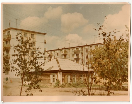 USSR - CIRCA 1970s: Vintage photo shows log cabin (log house) and blocks of flats in the background.のeditorial素材