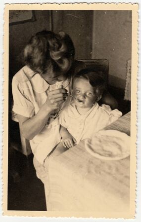HODONIN, THE CZECHOSLOVAK REPUBLIC - CIRCA 1942: A vintage photo shows small toddler girl and mother feeds her.のeditorial素材