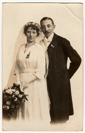 LIBEREC (REICHENBERG), THE CZECHOSLOVAK  REPUBLIC - CIRCA 1920s: Vintage photo of newlyweds with wedding bouquet. Bride wears wedding veil headdress. Groom wears posh clothing, white bow-tie. Black & white antique studio portrait.のeditorial素材