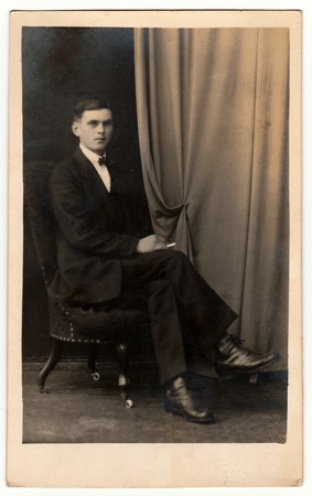 PRAGUE, THE CZECHOSLOVAK REPUBLIC - CIRCA 1920s: Vintage photo shows young man sits on armchair. Antique black & white studio portrait.のeditorial素材