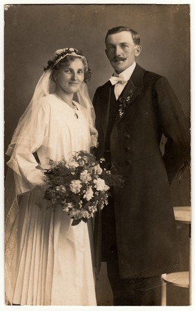 CHRASTAVA (KRATZAU), THE CZECHOSLOVAK  REPUBLIC - CIRCA 1920s: Vintage photo of newlyweds. Bride wears veil and she holds wedding bouquet.  Groom wears posh clothing, white bow-tie. Black & white antique studio portrait.のeditorial素材