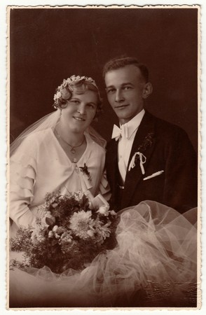 LIBEREC (REICHENBERG), THE CZECHOSLOVAK  REPUBLIC - CIRCA 1940s: Vintage photo of newlyweds with wedding bouquet. Bride wears wedding veil headdress. Groom wears posh clothing, white bow-tie. Black & white antique studio portrait.のeditorial素材