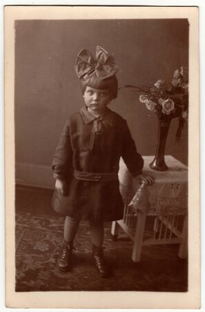 HAMBURG, GERMANY - CIRCA 1930s: Vintage photo shows a small girl wears hair ribbon, poses indoors....