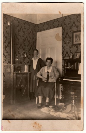 GERMANY - CIRCA 1930s: Vintage photo shows women pose at home. In the picture are piano and stove....