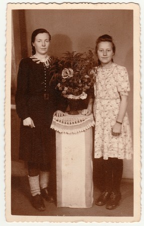 GERMANY - CIRCA 1930s: Vintage photo shows women pose in photo studio with bouquet on a white pedestal. Black & white antique photography.のeditorial素材