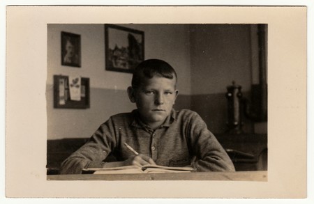 EILENBURG, GERMANY - CIRCA 1940s: Vintage photo shows young boy (pupil, student) sits at the classroom. Black & white antique photography.のeditorial素材