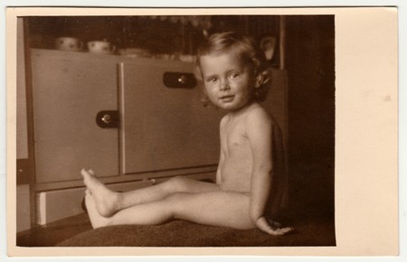 THE CZECHOSLOVAK REPUBLIC - JULY 12, 1942: Vintage photo shows a small boy - naked toddler. A cupboard is on the background. Retro black & white photography.のeditorial素材