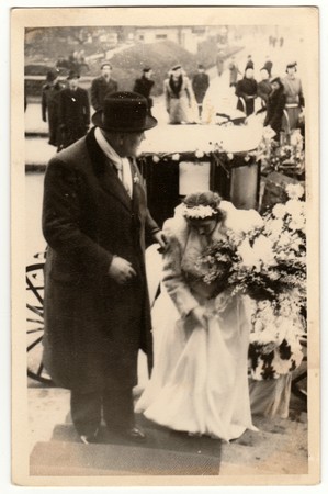 THE CZECHOSLOVAK REPUBLIC - CIRCA 1940s: Vintage photo shows a groom (bridegroom) and bride. A historical carriage (coach) is on the background. Retro black & white photography.のeditorial素材