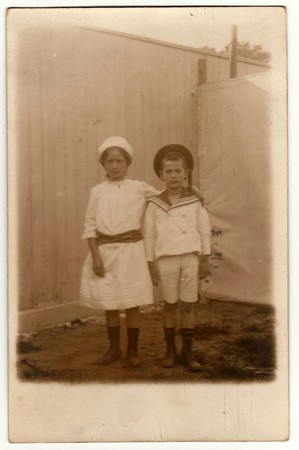 HAMBURG, GERMANY (DEUTSCHES REICH) - NOVEMBER 13, 1917: Vintage photo shows siblings (girl and boy) pose in the backyard. Boy wears a sailor costume and girl wears a white dress. Retro black & white photography.のeditorial素材