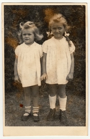 GERMANY - DECEMBER 23, 1946: Vintage photo shows two small girls (siblings). They wear a white dresses. Retro black & white photography.のeditorial素材