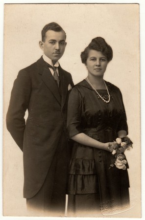 CHRASTAVA (KRATZAU), THE CZECHOSLOVAK REPUBLIC - CIRCA 1920s: Vintage photo shows a young couple wears black clothes. Woman holds flowers. Retro black & white photography.のeditorial素材