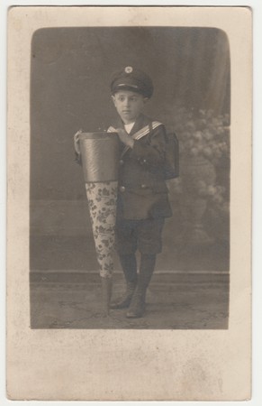 WALDENBURG, GERMANY - CIRCA 1920s: Vintage photo shows little boy with a School Cone ("Tute"), a big cardboard cone with toys, chocolate, candies, given the first day of school. Retro black & white studio photography.のeditorial素材