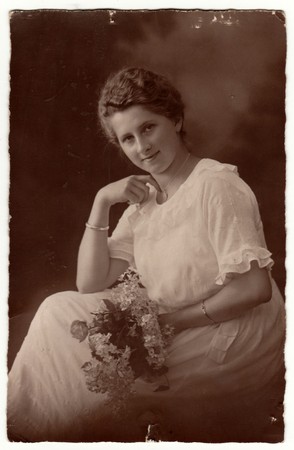 GERMANY - CIRCA 1920s: Vintage photo shows woman with short hair. Woman wears white dress and holds bouquet (bunch of flowers). Retro black & white studio photography with sepia effect.のeditorial素材