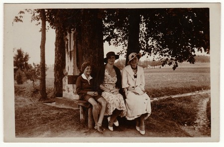THE CZECHOSLOVAK REPUBLIC - CIRCA 1930s: Vintage photo shows women wear  elegant dresses and women's parisisol big brim hat. The women and boy pose outdoors and sit on the bench. Retro black & white photography.のeditorial素材