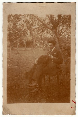 MALENICE NAD VOLYNKOU, THE CZECHOSLOVAK REPUBLIC - AUGUST 28, 1924: Vintage photo shows man sits on a chair in the garden. Retro black & white photography with sepia effect.のeditorial素材