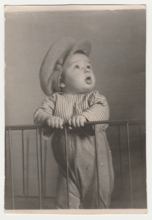 THE CZECHOSLOVAK SOCIALIST REPUBLIC - CIRCA 1960s: Vintage photo shows  a small cute boy stands in the cot. He wears a flat cap. Retro black & white photography.のeditorial素材