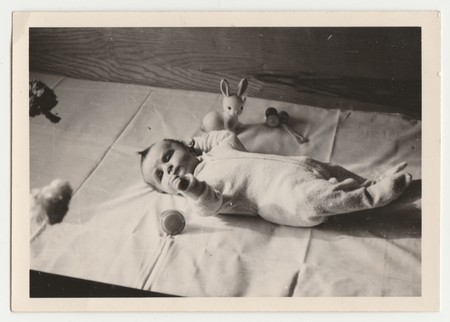 THE CZECHOSLOVAK SOCIALIST REPUBLIC - APRIL 4, 1970: Vintage photo shows a new born baby lies with toys. Retro black & white  photography.のeditorial素材