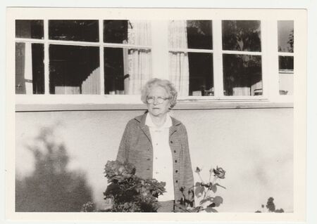 THE CZECHOSLOVAK SOCIALIST REPUBLIC - CIRCA 1980s: Vintage photo shows an older woman in front of country house. Retro black & white  photography.のeditorial素材