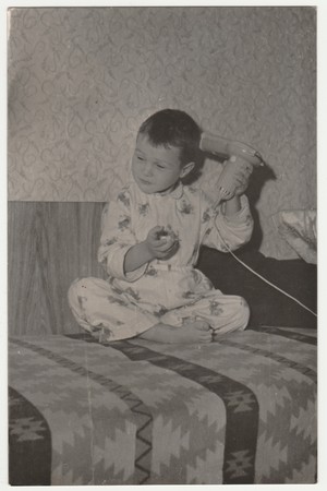 THE CZECHOSLOVAK SOCIALIST REPUBLIC - CIRCA 1970s: Vintage photo shows a small boy wears pyjamas and he uses hair dryer. Funny photography of a cute boy. Retro black & white  photography.のeditorial素材