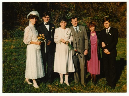 THE CZECHOSLOVAK REPUBLIC - CIRCA 1990s: Retro photo shows newlyweds and wedding guests pose outdoors. Bride wears white delicate wedding gown. She holds a small bouquet of golden roses. Vintage color photography.のeditorial素材