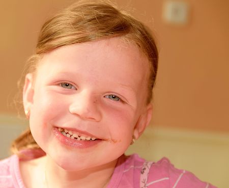 A cute small girl smiles. A small girl with chocolate cream stains on face. A small girl sits in the kitchen.の写真素材
