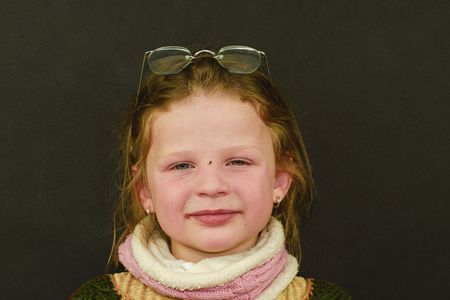Portrait of a small girl on black background. Girl wears retro glasses. Authentic and real photo.の写真素材