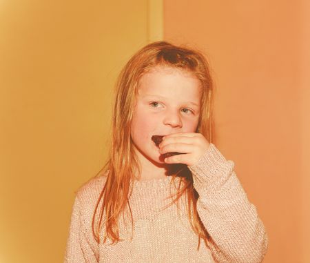 Portrait of girl. Blond girl posing indoor. Small girl is eating cookies. Add warm effect.の写真素材
