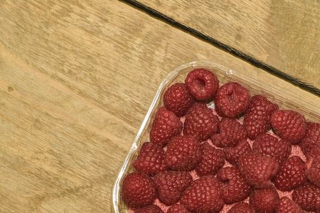 Red-fruited raspberries in plastic box on wooden background. Raspberries background. Close-up