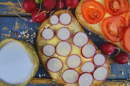 Spread butter on bread with sliced tomatoes and radishes. Fresh snack on natural wooden background. Flat design. Top viewの写真素材