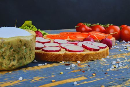 Spread butter on bread with sliced tomatoes and radishes. Fresh snack on natural wooden background