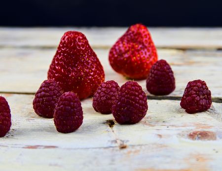 Strawberries and raspberries on rustic white wooden background. White and black background. Dark...